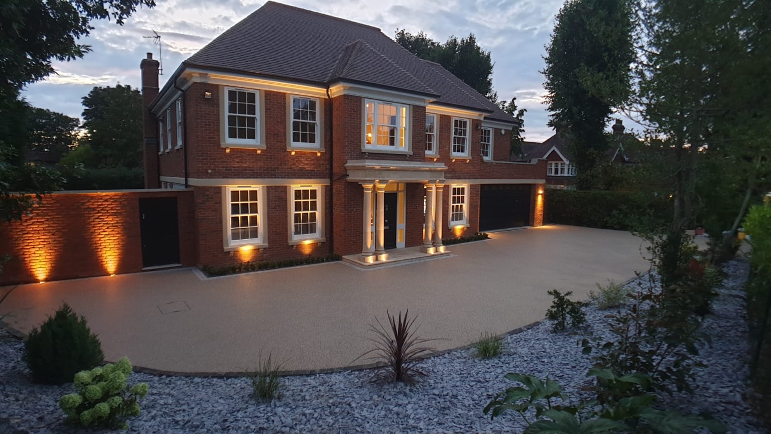 Resin driveway in front of a brick house with warm exterior lighting at dusk